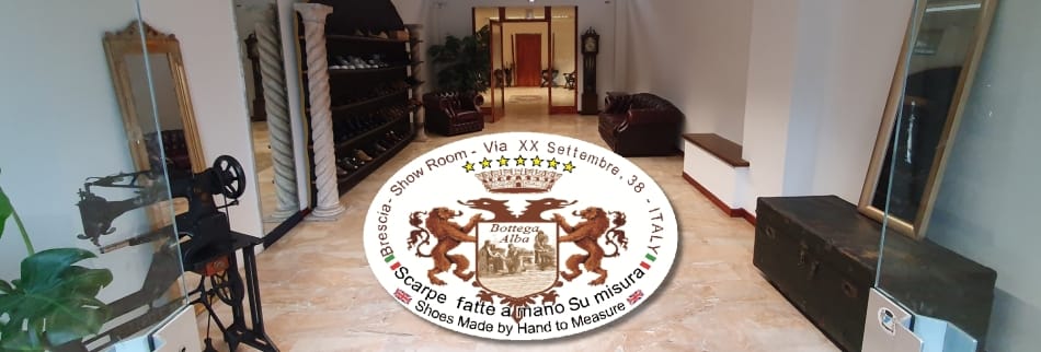 Ingresso dell'atelier di Brescia: pavimento in marmo chiaro, scaffali con calzature esposte, macchina da cucire d'epoca
