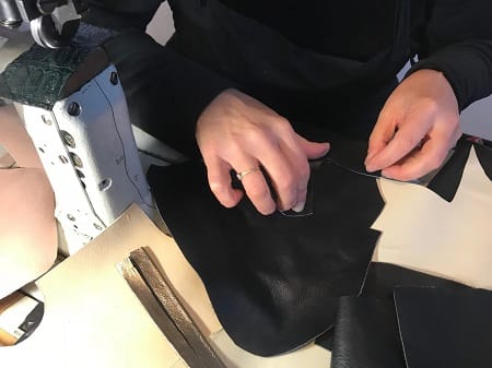 Rifilatura a mano di una tomaia in pelle nera al banco, accanto alla macchina da cucire