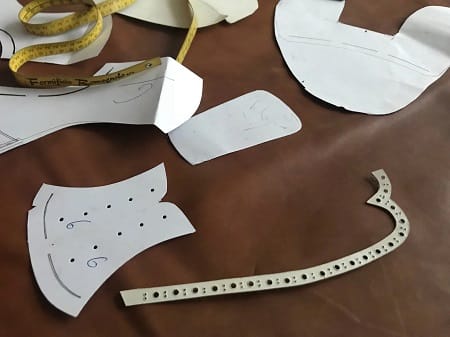 Cartamodelli e un contrafforte forato per la stringatura su una pelle marrone, con il metro da sarto
